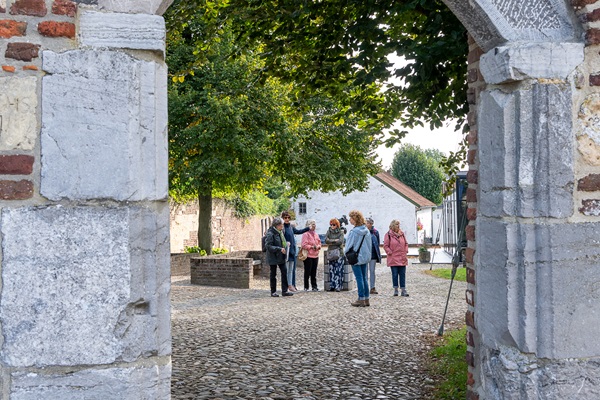 Groep krijgt een rondleiding door een gids in Thorn gezien door een openstaande poort in de vestingsmuur