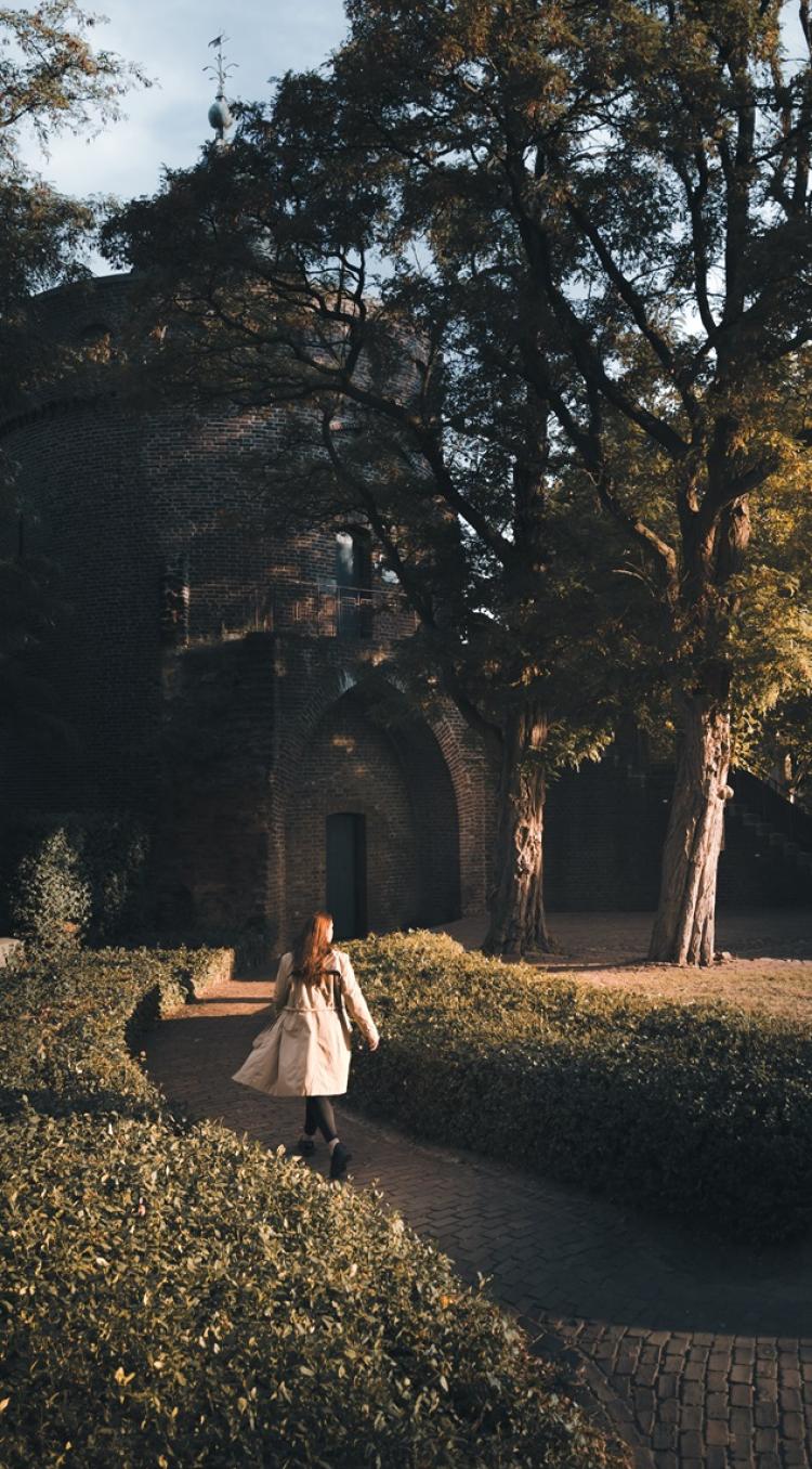 Vrouw wandelt ontspannen langs de Rattentoren in Roermond, omgeven door warme herfstkleuren.