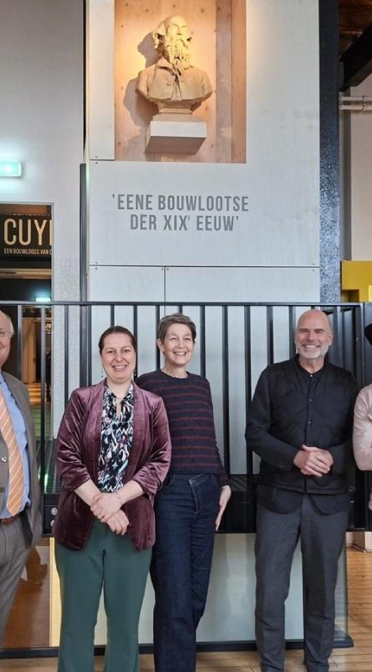 Groepsfoto van vijf lachende personen in de hal van het Cuypershuis in Roermond, onder een buste van architect Pierre Cuypers.
