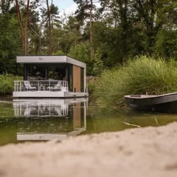 Loo mare, een modern floating tiny house met wellness, dobberend op een bosmeer, omringd door groen en rust, met zandstrand op de voorgrond.