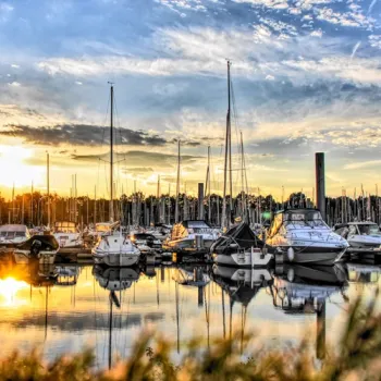Jachthaven met zeilboten en motorboten bij zonsondergang, met spiegeling van de lucht in het water.